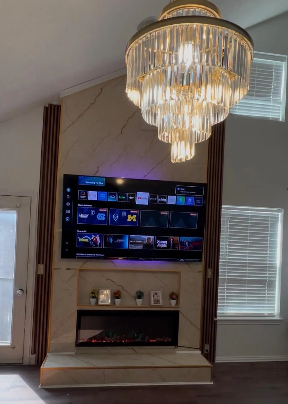 The finished wall in porcelain slab with fluted walnut returns, a mounted display, linear fireplace and chandelier