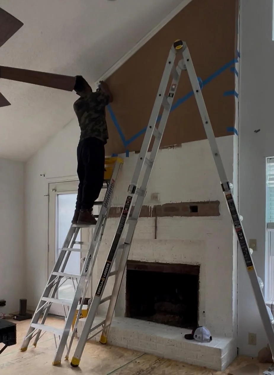 Living room mid-demolition: the old white brick fireplace exposed, ladders up against the chimney breast