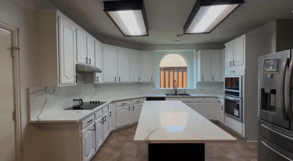 White kitchen with a large quartz island, double wall ovens and an arched window over the sink