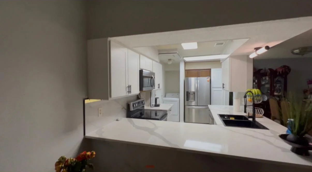 The same kitchen opened up, with white cabinetry and a quartz peninsula with a waterfall return