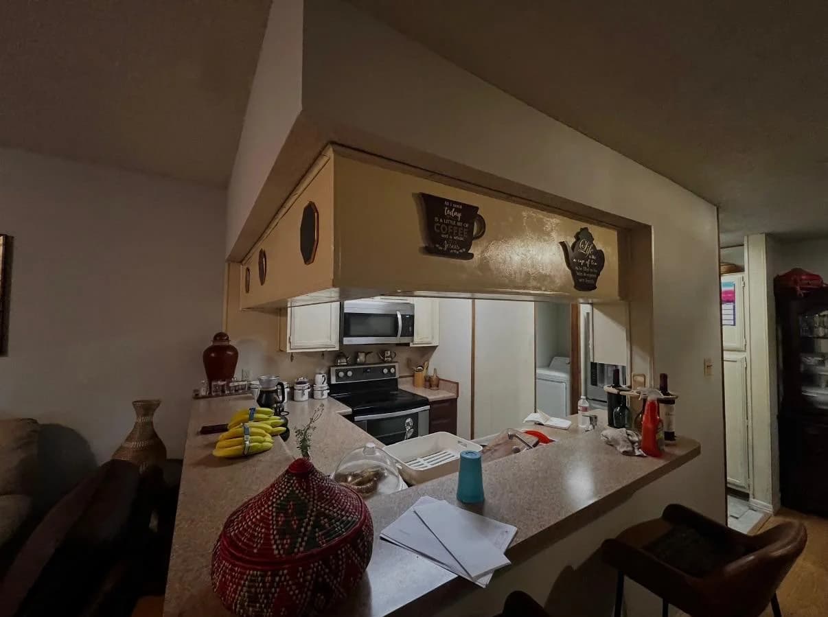 The original closed kitchen: dark bulkhead over the pass-through, dated tile counters and cluttered worktops