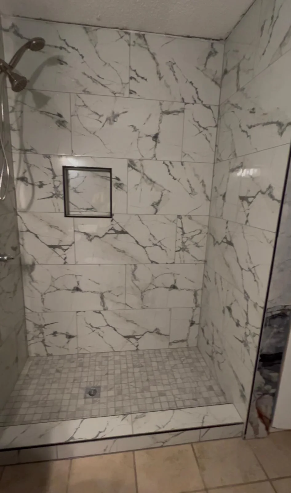 The finished walk-in shower tiled in marble-look porcelain with a mosaic pan and recessed niche
