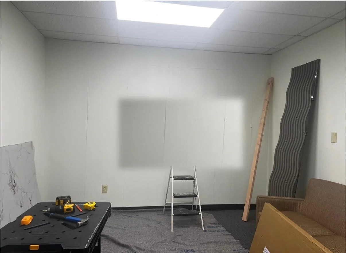 The bare office wall before work, with materials and a step ladder stacked against it
